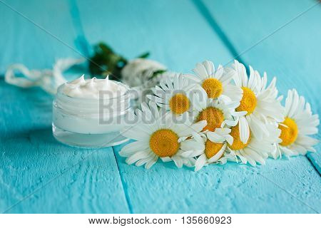 Cosmetic cream with camomile flower for a body and face on blue wooden table.