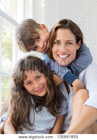 Son and daughter embracing mother. Mother enjoying with children on a bright sunny morning. Portrait of happy smiling mom with her children at home looking at camera. Happy family embracing.