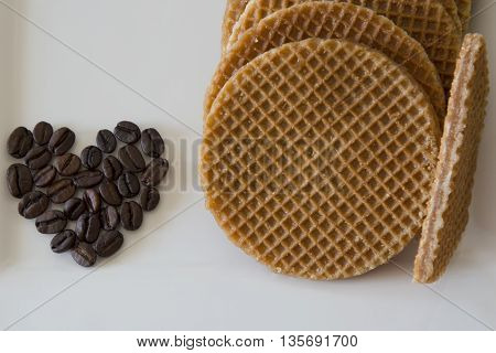 Coffee beans in a heart shape besides soft toasted dutch waffles filled with caramel