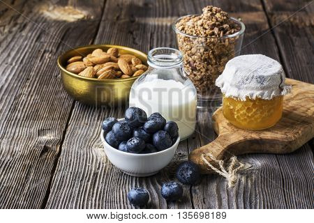 Healthy breakfast ingredients. Cereal, chocolate muesli, fresh blueberries, jar with honeycombs, rustic milk bottle on a simple plank dark background in rustic style. selective focus
