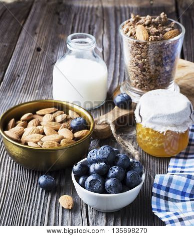 Healthy breakfast ingredients. Cereal, chocolate muesli, fresh blueberries, jar with honeycombs, rustic milk bottle on a simple plank dark background in rustic style. selective focus