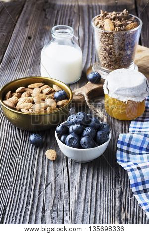 Healthy breakfast ingredients. Cereal, chocolate muesli, fresh blueberries, jar with honeycombs, rustic milk bottle on a simple plank dark background in rustic style. selective focus