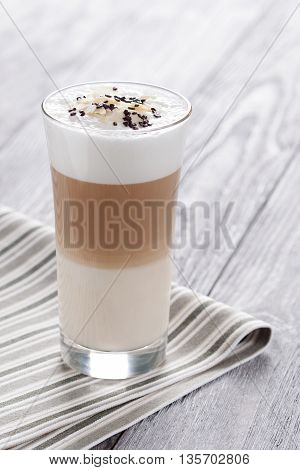 Sweet coffee with milk served in glass. Latte macchiato decorated with pinch of cacao and almonds flakes.