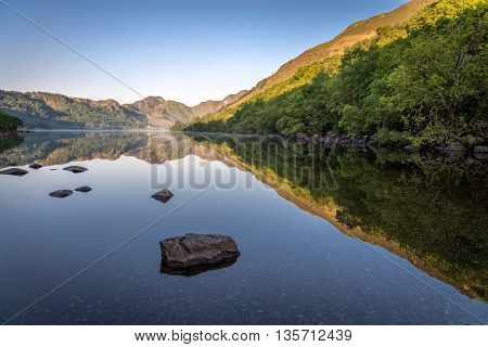 Perfectly symmetric reflections on a mirror-like lake at sunrise, rocks in foreground