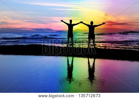 Silhouette of a gay couple on the beach with a rainbow sunset.