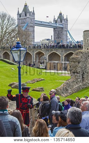 LONDON UK - APRIL 10TH 2016: A Yeomen Warder talking to visitors during a tour of the historic Tower of London on 10th April 2016. Tower Bridge can be spotted in the background.