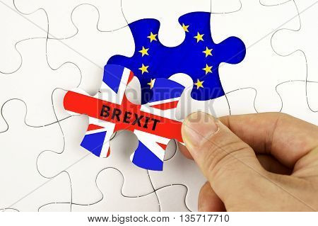 Hand Holding Piece Of Jigsaw Puzzle With The Flag Of European Union And Word Brexit On Great Britain