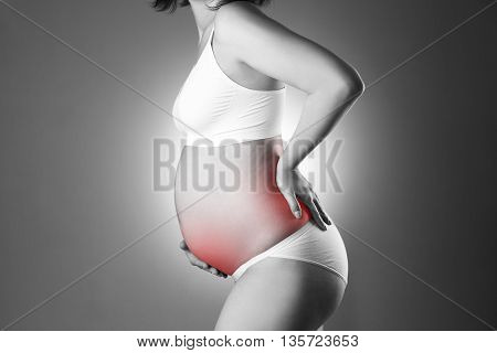 Caucasian pregnant woman in white lingerie with back and abdominal pain on gray studio background. Pregnancy concept