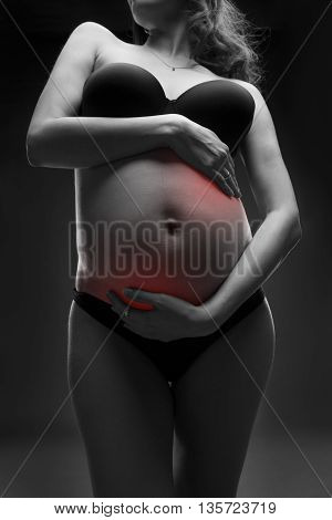 Caucasian pregnant woman in black lingerie with abdominal pain on gray studio background. Pregnancy concept