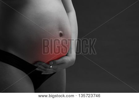 Caucasian pregnant woman in black lingerie with abdominal pain on gray studio background. Pregnancy concept with copy space