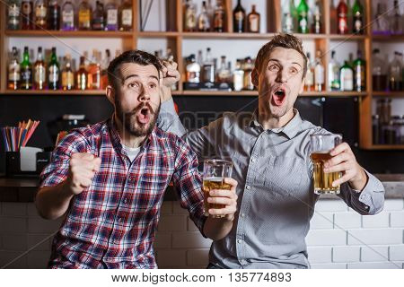 Young fun people with beer watching football in a bar