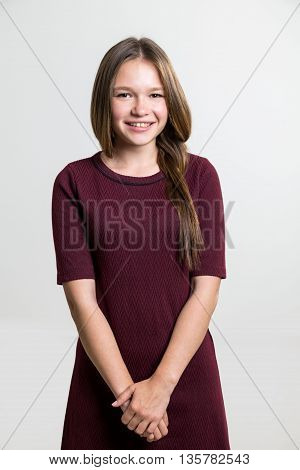 Portrait of cute cheerful young female in vinous dress on light grey background