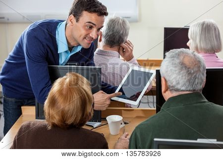 Smiling Teacher Showing Digital Tablet To Senior Students In Cla