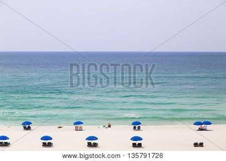 PENSACOLA BEACH, USA - MAY 13, 2015: The beach with a few people sunbathing and relaxing with beach chairs and sunshades looking towards the horizon above the calm sea.
