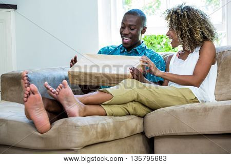 Excited couple sitting on sofa and opening a parcel at home