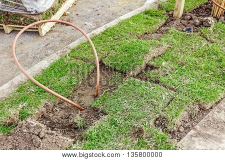Bended copper pipe is coming out from the ground around grass roots.