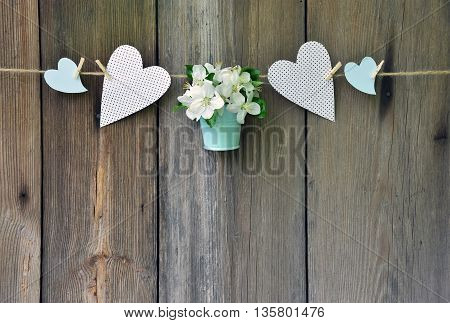 Blooming apple tree in a blue basket and colorful hearts on old wooden background. Wedding decoration in a rustic style. Rustic style. Celebration. Love. Greeting. Spring.