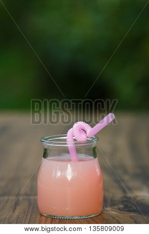 jar of cold pink cocktail with straw on green background bokeh