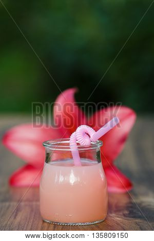 jar of cold pink cocktail with straw on green background bokeh