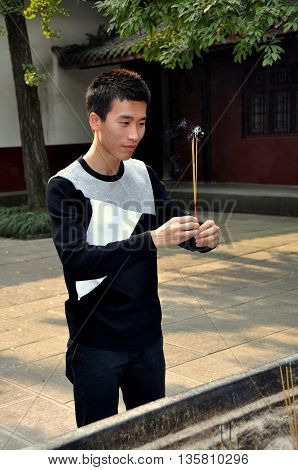 Chengdu China - November 8 2010: Young Chinese man holding burning incense sticks prays in a quiet courtyard at the 17th century Wenshu Buddhist temple