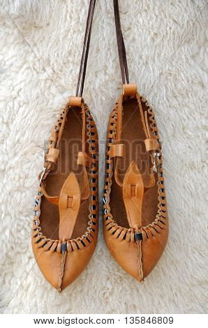 Pair of traditional Bulgarian leather shoes agaisnt white lambskin background