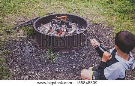 Young boy cooking hot dog on a outdoor camp fire.