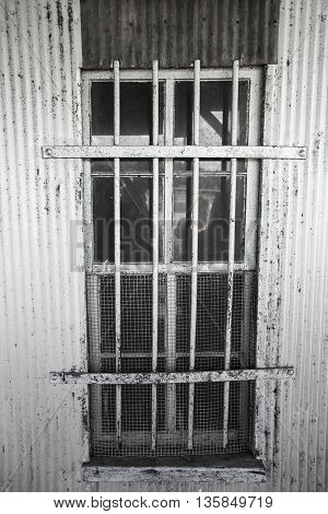 A scary looking window with bars and a mesh screen on a metal building perhaps a jail or prison