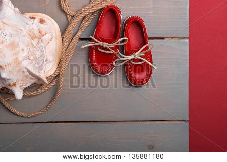 Red boat shoes near big shell and rope on wooden background. Top view/. Copy space. Frame.