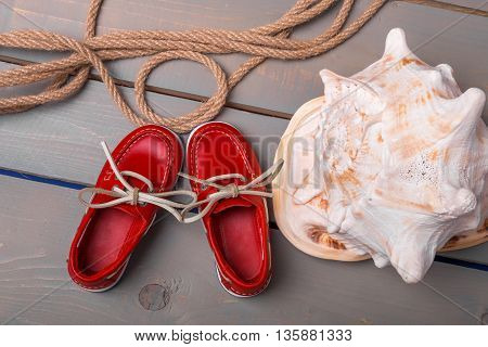 Red boat shoes near big shell and rope on wooden background. Close up. Top view.