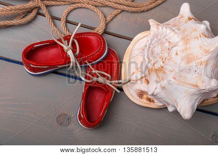 Red boat shoes near big shell and rope on wooden background. Close up. Top view.