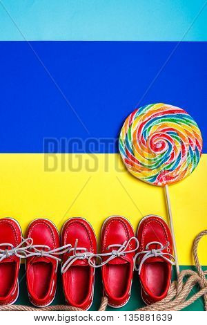 A lot of small red boat shoes near big multi-colored lollipop on colored background. Top view copy space. Frame. group of child boat shoes.