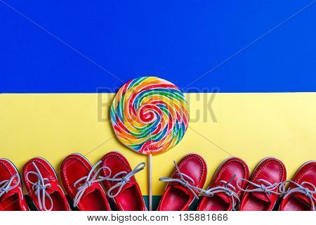 A lot of small red boat shoes near big multi-colored lollipop on colored background. Top view copy space. Frame. group of child boat shoes.
