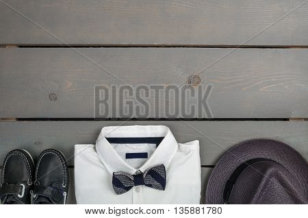 Men's outfit on wooden background. Kids fashion clothes. Grey fedora white shirt black bow tie and boat shoes for boy. Top view. Copy space. Frame