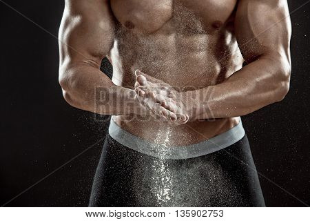 young muscular man preparing to hand lifting heavy weight. White talcum dynamically scatters in different directions. Close-up