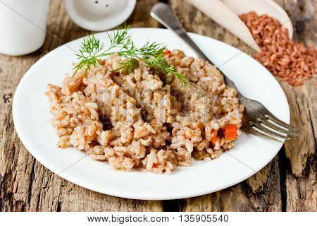 Delicious and healthy pilaf of medium-grain red matta (devzira) rice on old wooden table selective focus