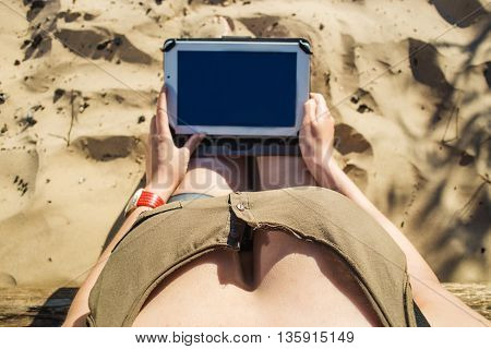 Top view shot of a busty woman holding digital tablet with a blank screen - closeup, fem a hands holding blank digital tablet against sand in sunlight. Focus on beautiful breasts