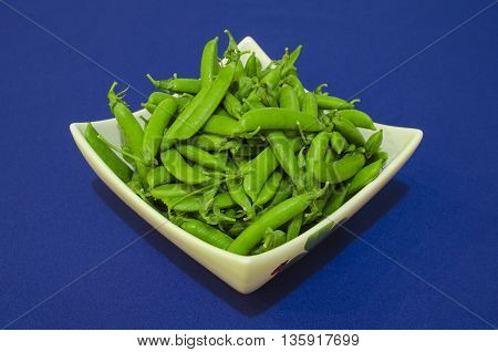 Fresh green peas in white dish on a blue background