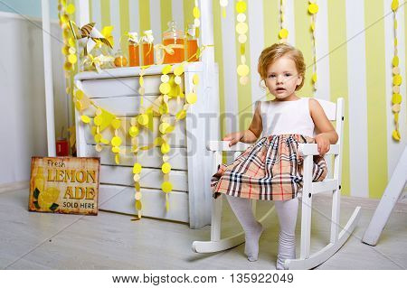 Beautiful little girl.Blue-eyed blonde.White chair.Lemonade.Children's room. Happy small girl portrait.