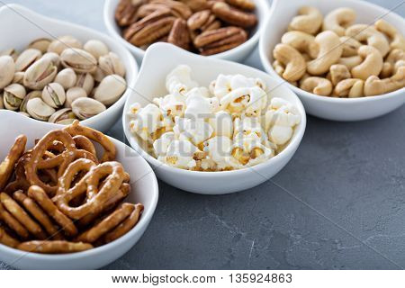 Variety of healthy snacks in white bowls pretzels and nuts