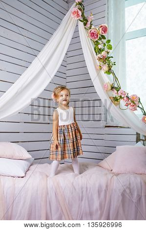 Beautiful little girl jumping on bed. Blue-eyed blonde.Children's room. Happy small girl portrait.