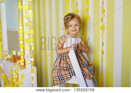 Beautiful little girl sitting on step ladder.Blue-eyed blonde.Children's room. Happy small girl portrait.