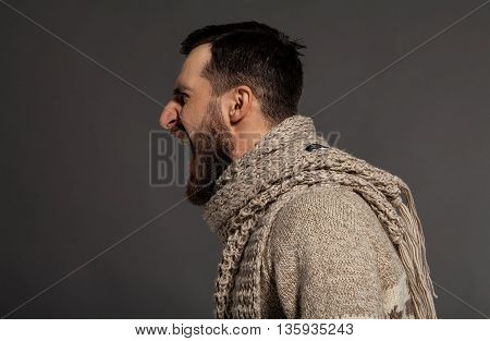 Unleashing his emotions. Side view of furious young bearded man shouting while standing against grey background