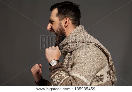 Unleashing his emotions. Side view of furious young bearded man shouting while standing against grey background