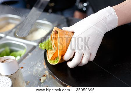 Making vegetable crepe, roll with tomatoes and lettuce. Salty crepe or pancake with fillings made by street vendor's hands at outdoors creperie. French cuisine, cooking for commercial kitchen.