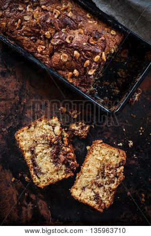 Top view of banana bread with Nutella swirl and chopped hazelnuts on a dark background. Dark food photography.