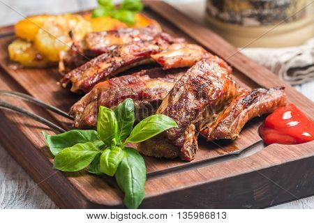 elicious Grilled Pork Rib and Fried Potato Wedges with Sauce on wooden cutting board, white wooden background