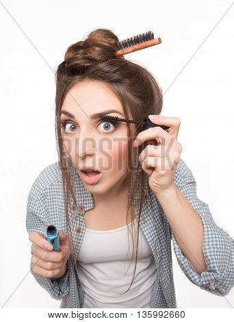 Hipster woman painting her eyeslashes over white background. Beautiful lady with hairstyle doing makeup in studio.