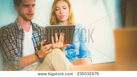 Young couple moving in new home.Sitting and relaxing after unpacking.Looking something on laptop. Young couple