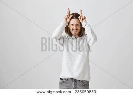 Handsome Guy Showing His Temper. Funny Good-looking European Male Model Showing Horns With Index Fin