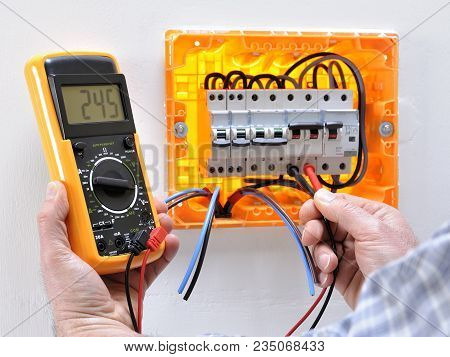 Electrician Technician Working On A Residential Electrical Panel, Measures The Voltage On The Termin